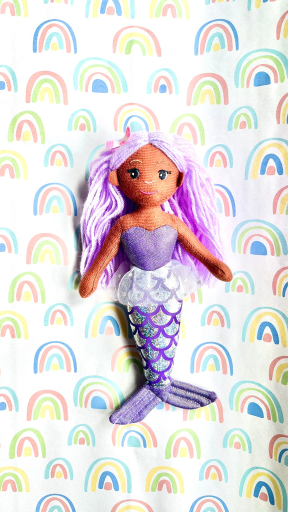 Mermaid doll with purple hair and tail on a rainbow-patterned background
